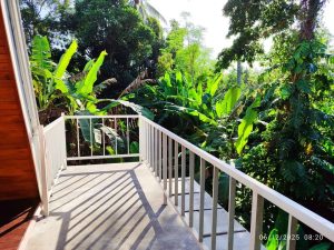 Balkon kabin kayu segitiga 2 kamar tidur di tengah taman hijau.
