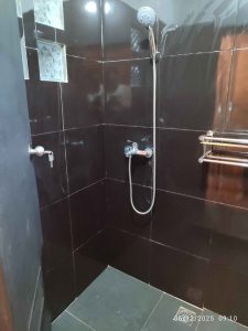Kamar mandi rumah kayu segitiga dengan shower dan akses mudah.