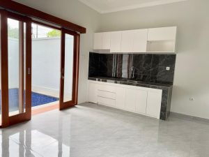 Dapur modern minimalis di villa Sanur dengan akses pintu kaca ke taman luar.
