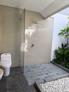 Area mandi terbuka di villa dekat Canggu, Bali, dengan desain minimalis dan pemandangan taman hijau.