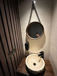 Wastafel batu alam unik di kamar mandi modern, dilengkapi cermin bulat dan keran hitam elegan.